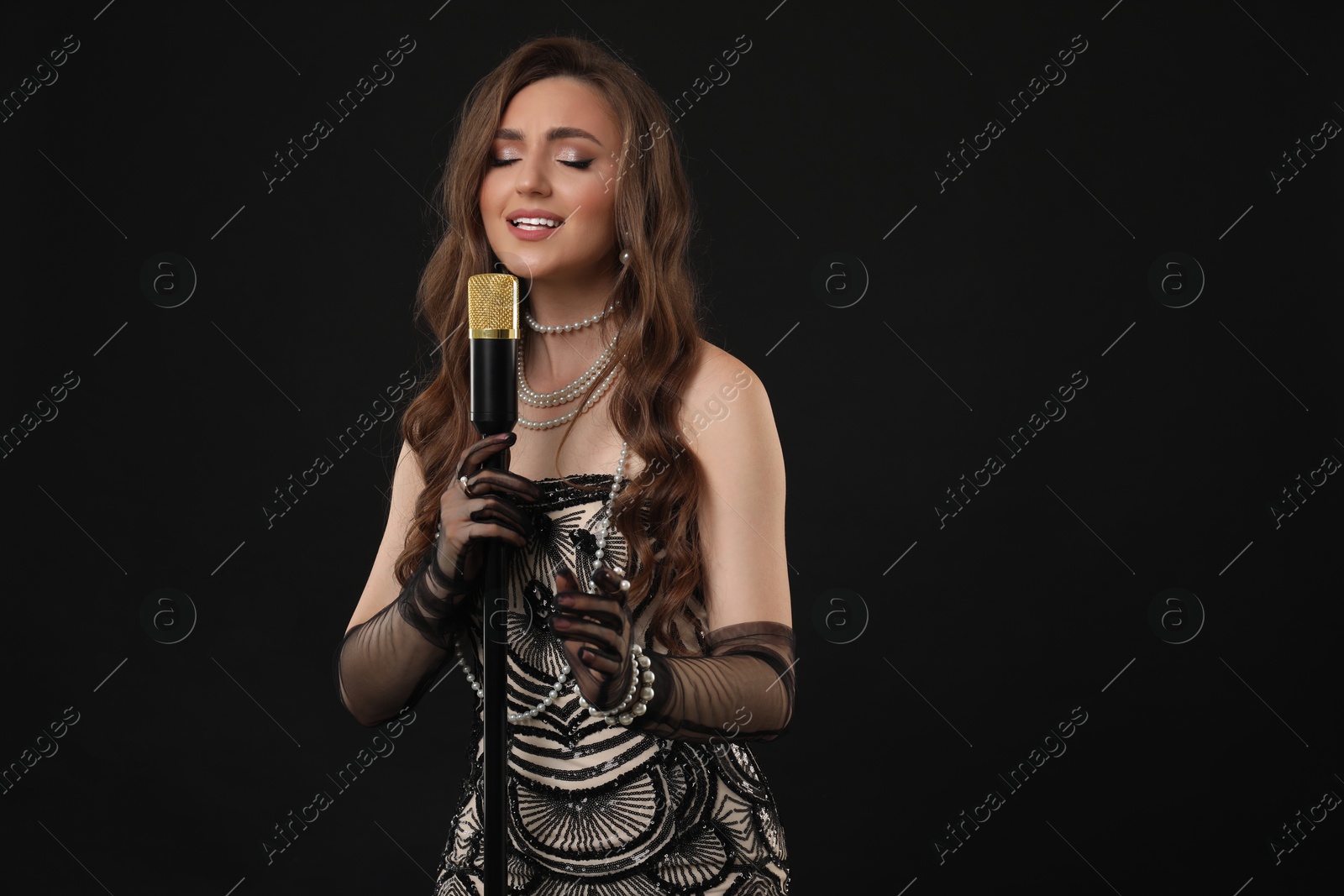 Photo of Beautiful young woman in stylish dress with microphone singing on black background