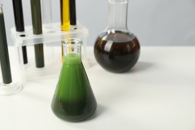 Photo of Laboratory glassware with different types of oil on white table, closeup. Space for text