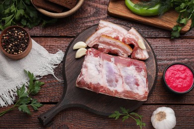 Photo of Pieces of pork fatback served with sauce and spices on wooden table, flat lay