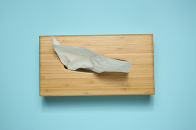 Photo of Wooden holder with paper tissues on light blue background, top view