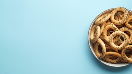 Photo of Bowl with delicious ring shaped Sushki (dry bagels) on light blue background, top view. Space for text