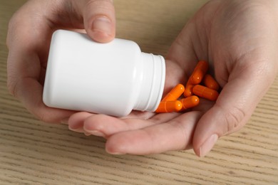 Woman pouring pills from bottle at wooden table, closeup