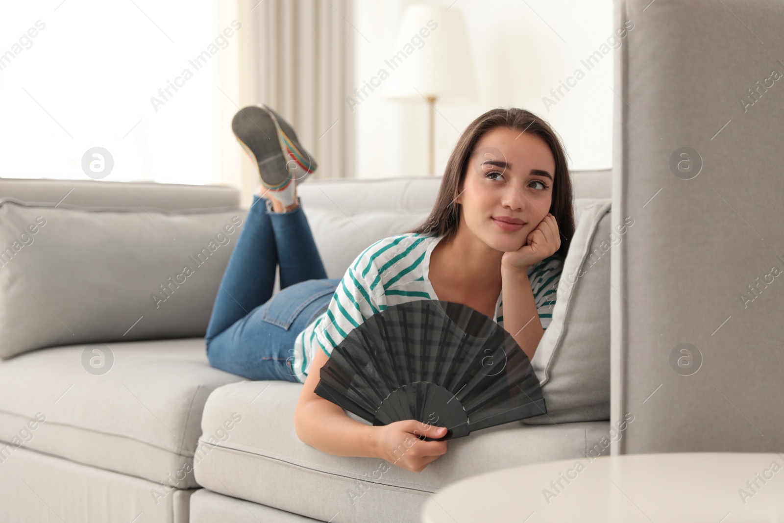 Photo of Woman enjoying air flow from hand fan at home. Summer heat