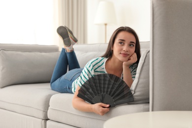 Woman enjoying air flow from hand fan at home. Summer heat