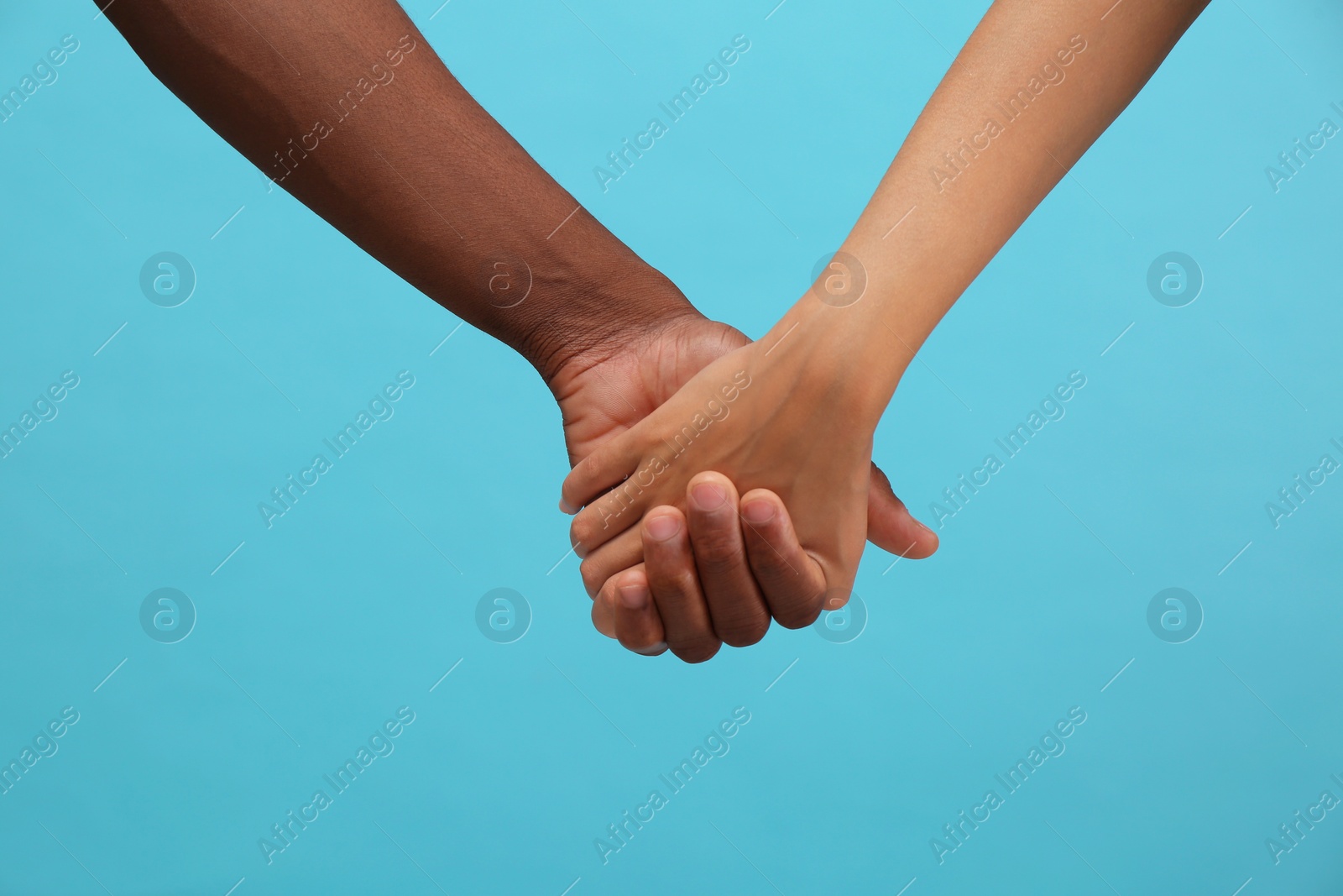 Photo of Woman and African American man holding hands on light blue background, closeup
