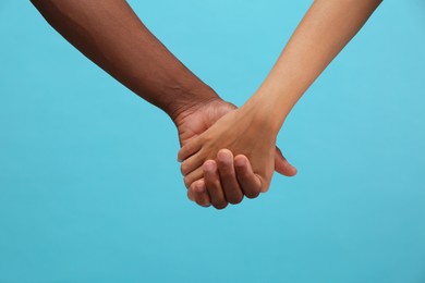 Photo of Woman and African American man holding hands on light blue background, closeup