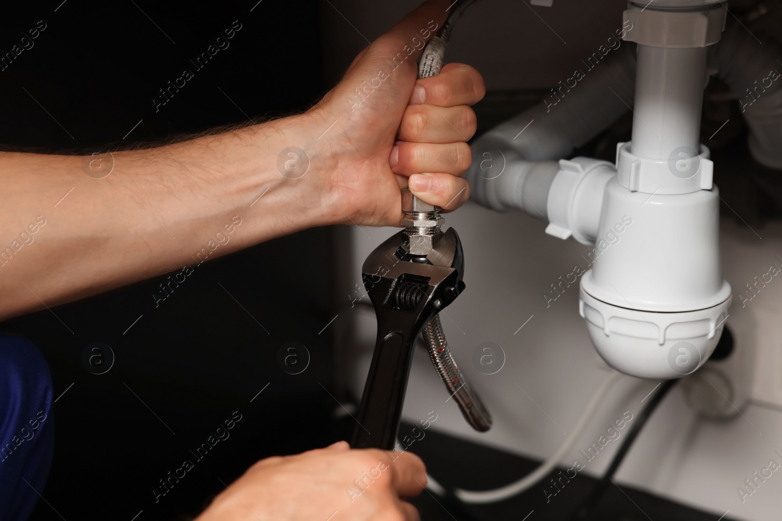 Photo of Professional plumber with adjustable wrench fixing sink, closeup