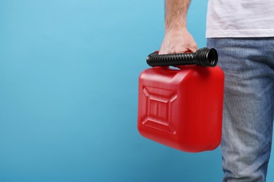 Man holding red canister on light blue background, closeup. Space for text
