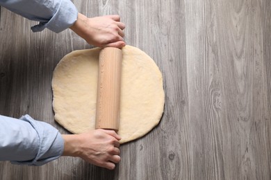 Photo of Woman rolling raw dough at wooden table, top view. Space for text