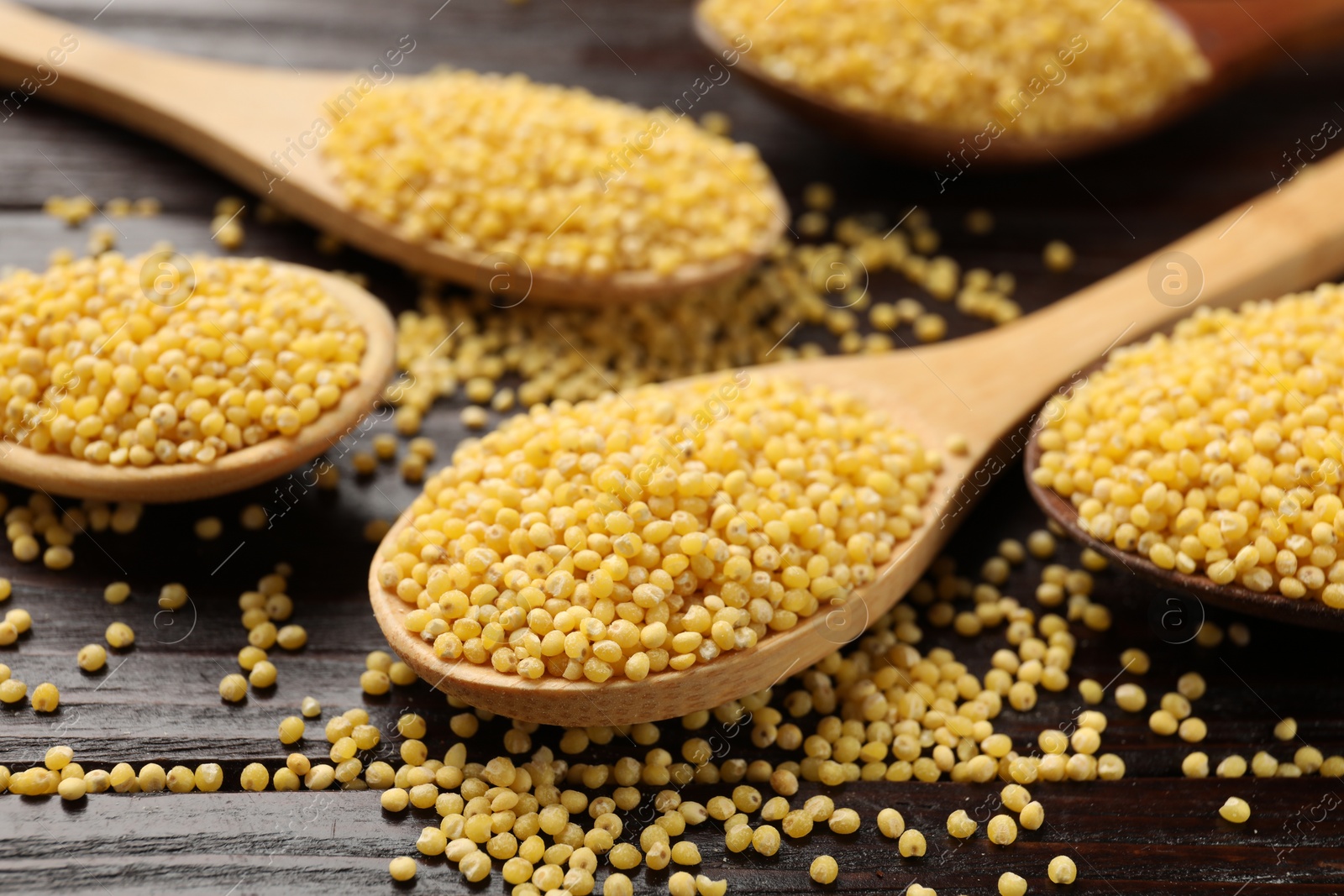 Photo of Spoons with millet groats on wooden table, closeup