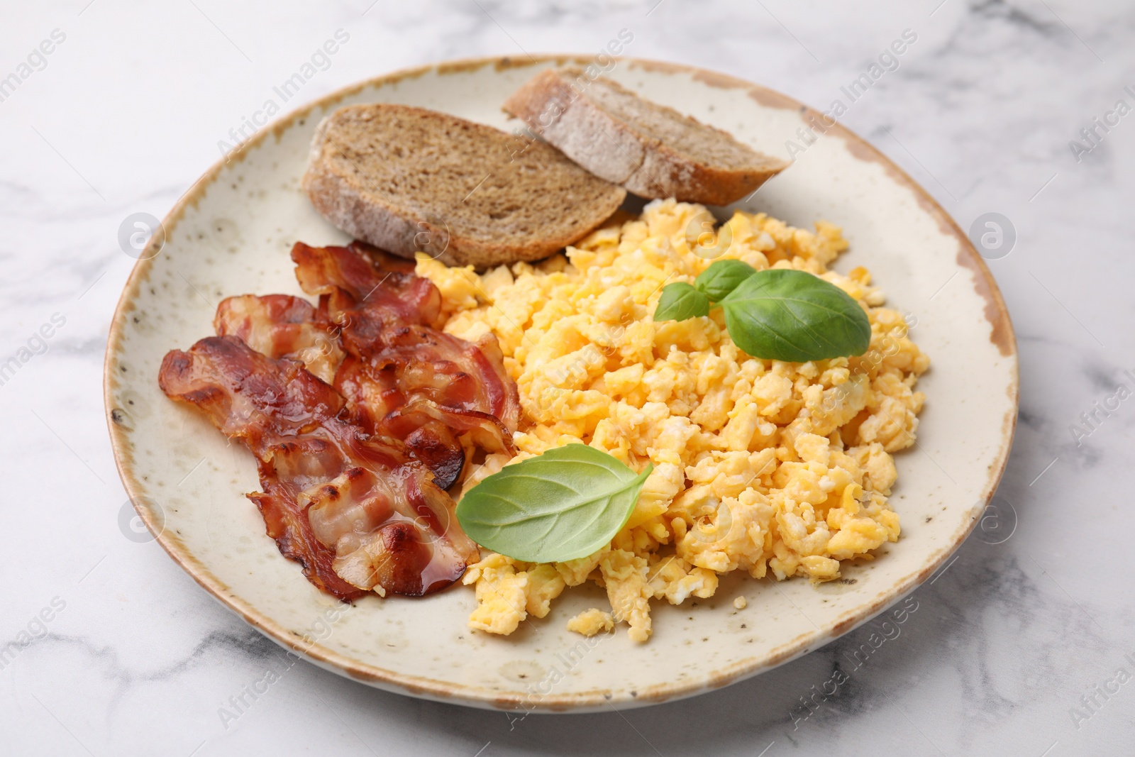 Photo of Delicious scrambled eggs with bacon and basil in plate on white marble table