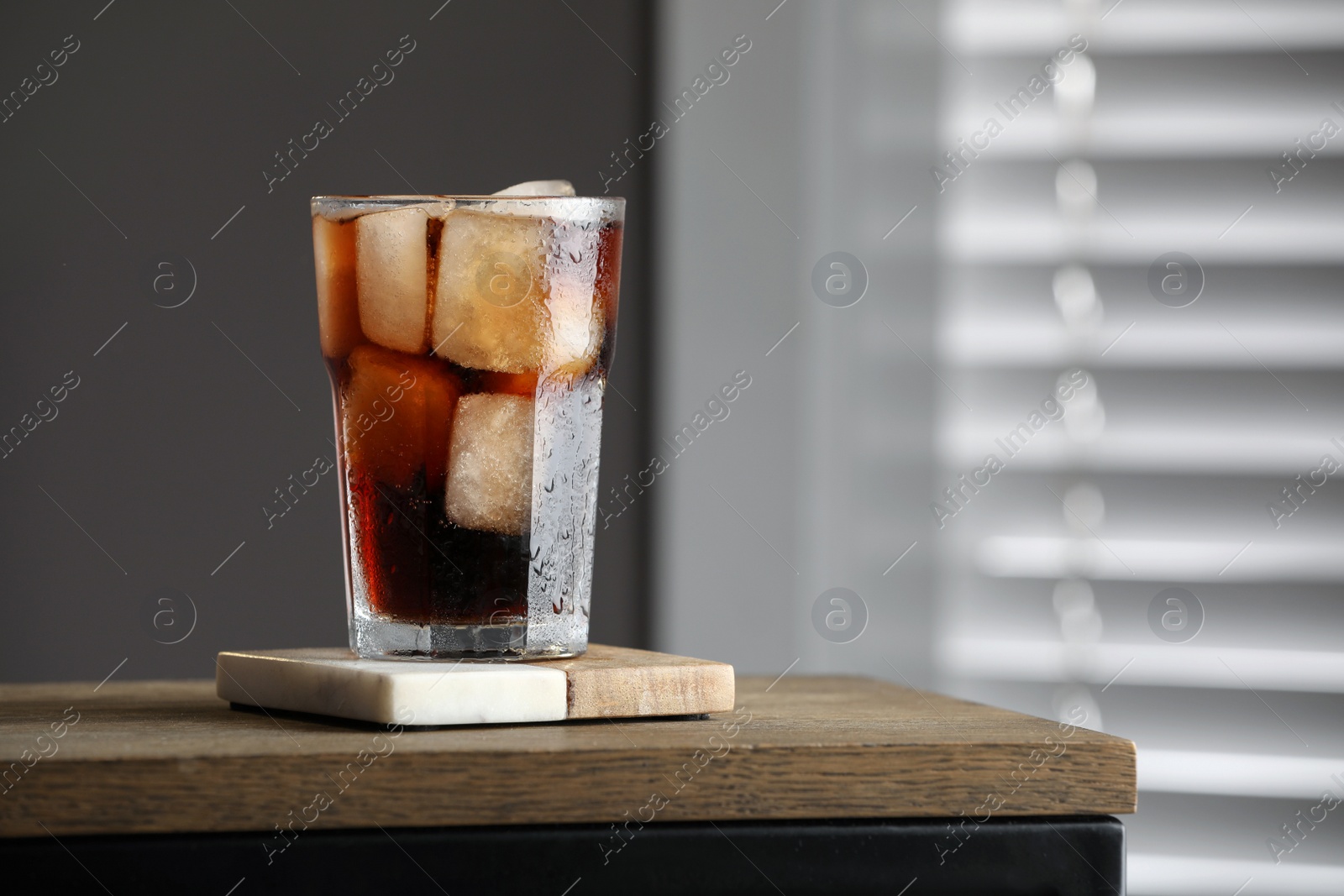 Photo of Glass of cold drink and stylish cup coaster on wooden table in room. Space for text