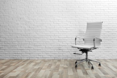 Comfortable office chair near white brick wall indoors. Space for text