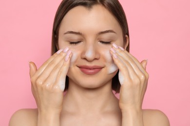 Photo of Young woman washing face with cleansing foam on pink background. Skin care cosmetic