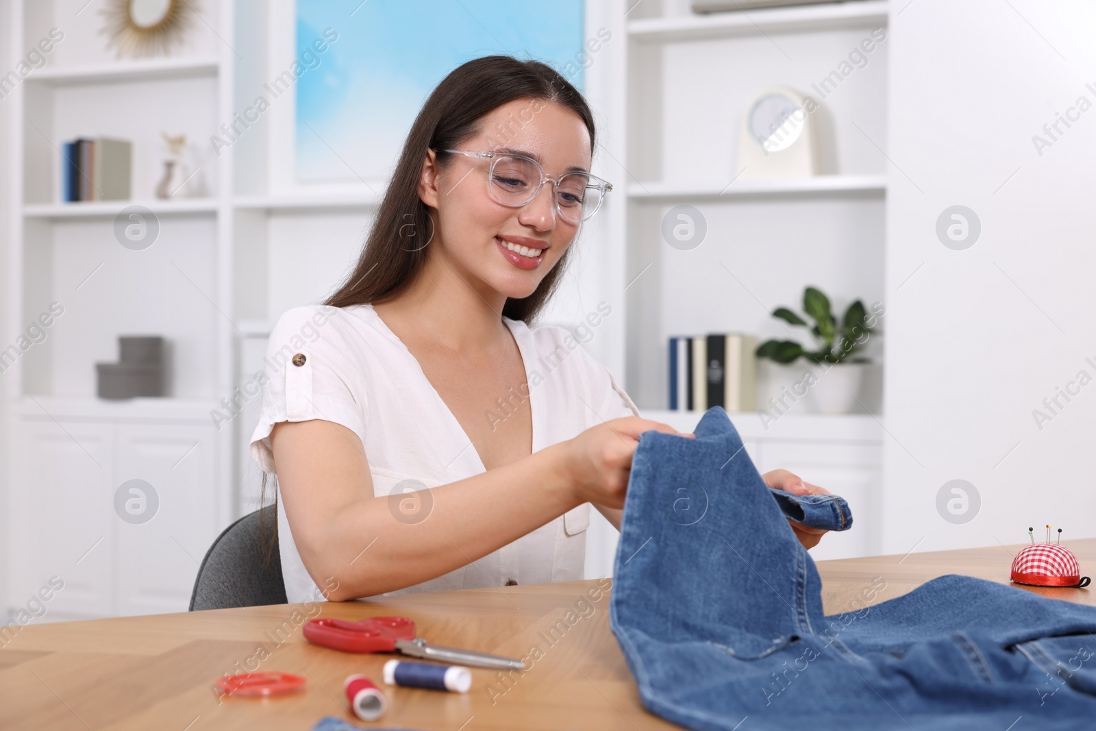 Photo of Happy woman holding jeans and cut hem at table indoors