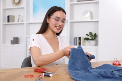 Photo of Happy woman holding jeans and cut hem at table indoors