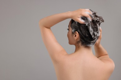Photo of Woman washing hair on grey background, back view. Space for text