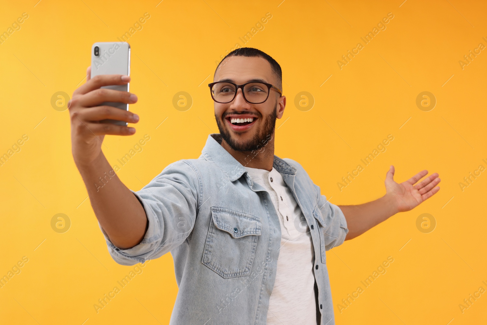 Photo of Smiling young man taking selfie with smartphone on yellow background