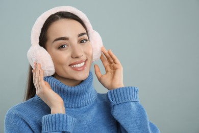 Photo of Beautiful young woman wearing earmuffs on light grey background. Space for text