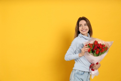 Photo of Happy woman with red tulip bouquet on yellow background, space for text. 8th of March celebration