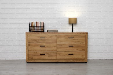 Photo of Wooden chest of drawers, books and lamp near white brick wall. Interior design