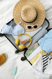 Open suitcase full of clothes, slippers and summer accessories on bed, flat lay
