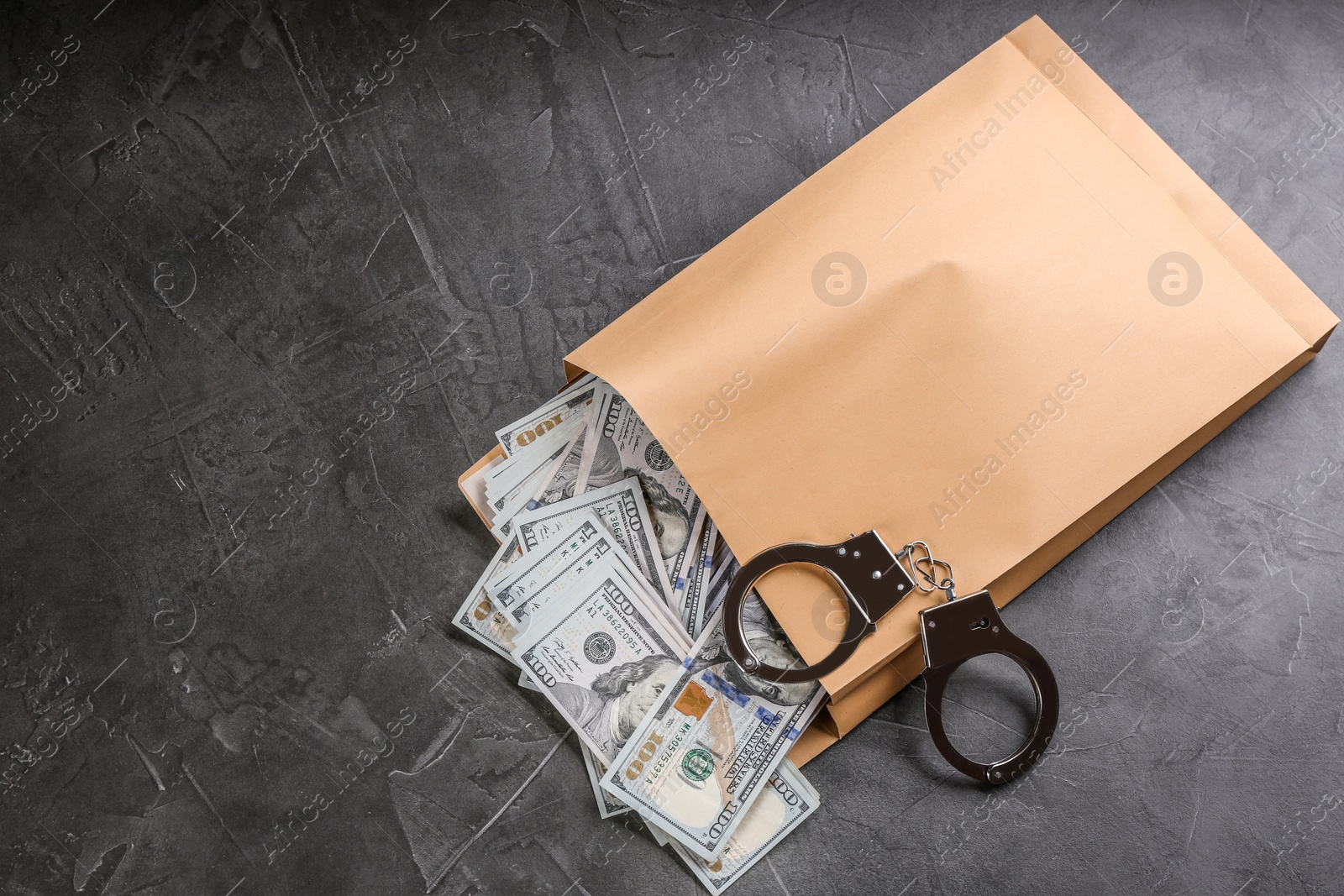 Photo of Envelope with dollar bills and handcuffs on grey stone table, top view. Bribe concept