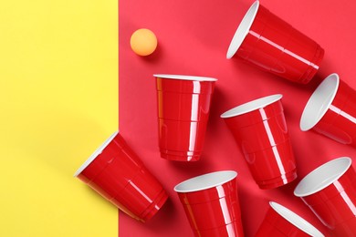 Photo of Plastic cups and ball on color background, flat lay. Beer pong game
