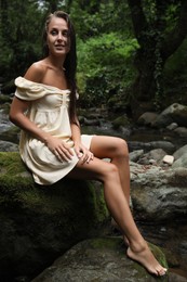 Photo of Beautiful young woman sitting on rock near mountain river in forest