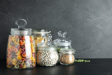 Photo of Glass jars with different types of groats and pasta on black table