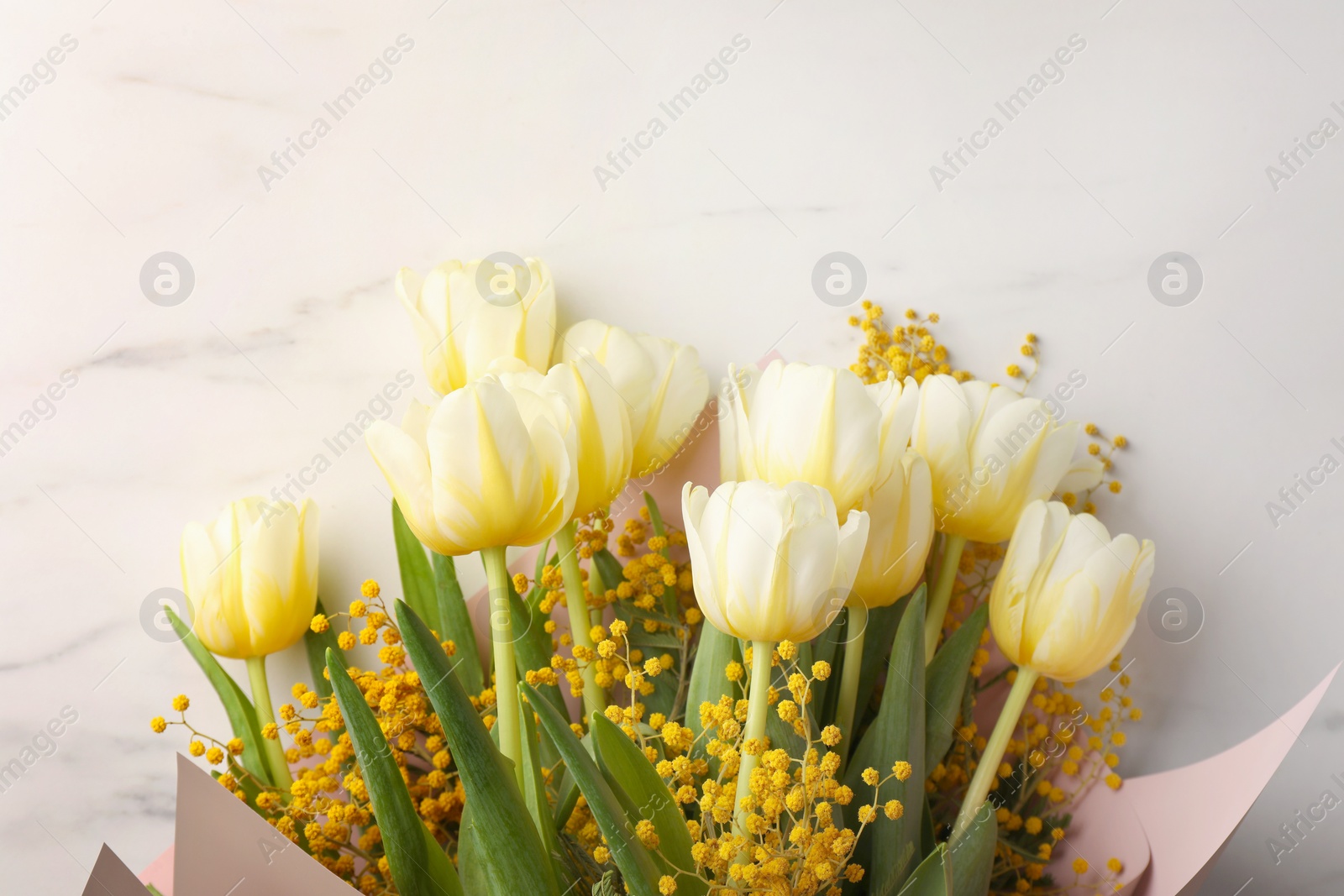 Photo of Bouquet with beautiful tulips and mimosa flowers on white marble table, top view