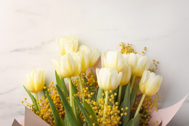 Bouquet with beautiful tulips and mimosa flowers on white marble table, top view