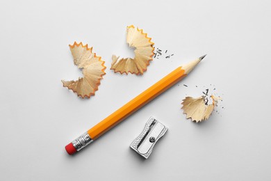 Photo of Graphite pencil, shavings and sharpener on white background, flat lay