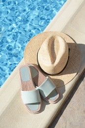 Photo of Stylish slippers and straw hat at poolside on sunny day. Beach accessories