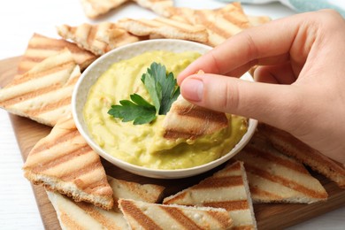 Woman dipping pita chip into hummus at table, closeup