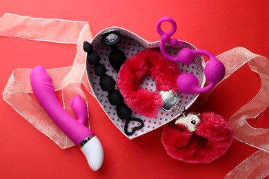 Photo of Gift box with different sex toys on red background, flat lay