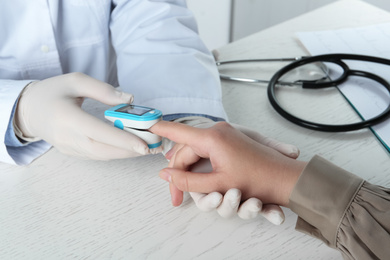 Photo of Doctor examining patient with fingertip pulse oximeter at white wooden table, closeup