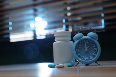 Photo of Alarm clock and pills on table indoors, space for text. Insomnia treatment