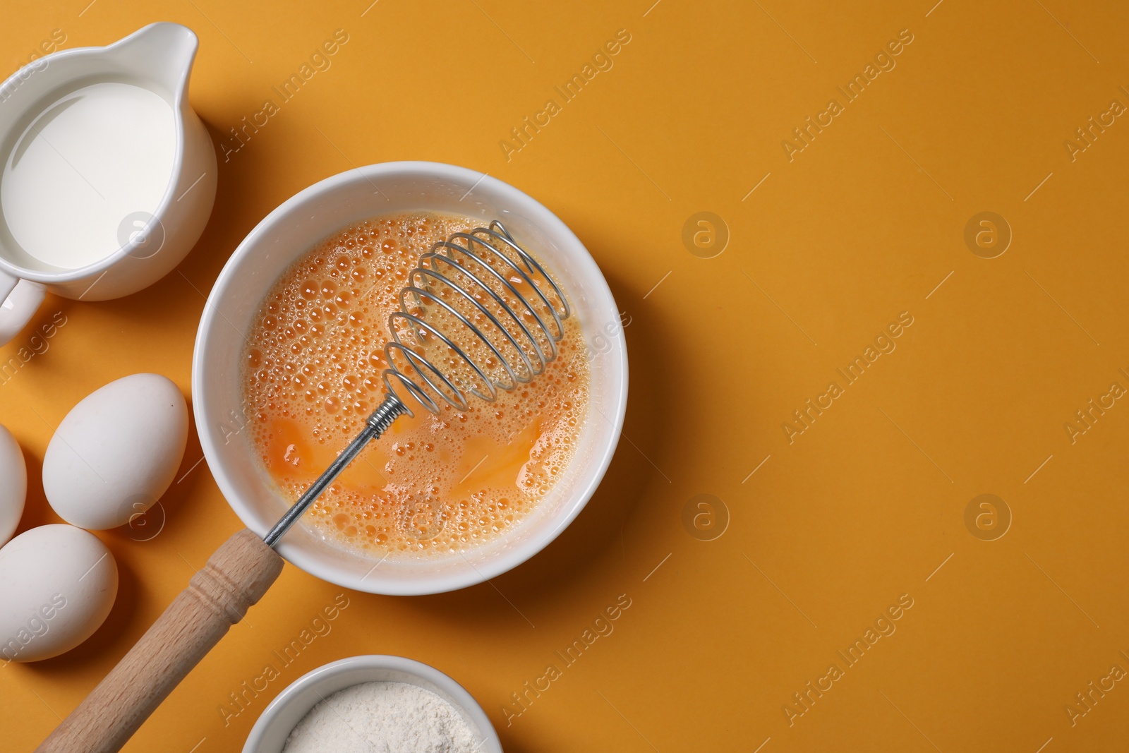 Photo of Making dough. Beaten eggs in bowl, flour and milk on orange background, flat lay. Space for text