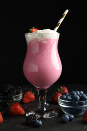 Photo of Tasty milk shake with whipped cream and fresh berries on black slate table