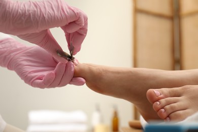 Photo of Professional pedicurist cutting client`s toenails with clipper in beauty salon, closeup