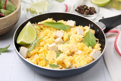 Photo of Frying pan with delicious scrambled eggs, tofu and lime on white table, closeup