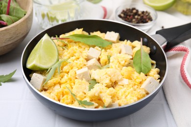 Frying pan with delicious scrambled eggs, tofu and lime on white table, closeup