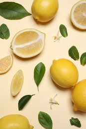 Many fresh ripe lemons with green leaves and flowers on beige background, flat lay