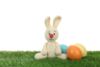 Cute Easter bunny toy and dyed eggs on green grass against white background