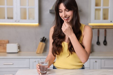 Beautiful woman taking vitamin pill at white marble table in kitchen