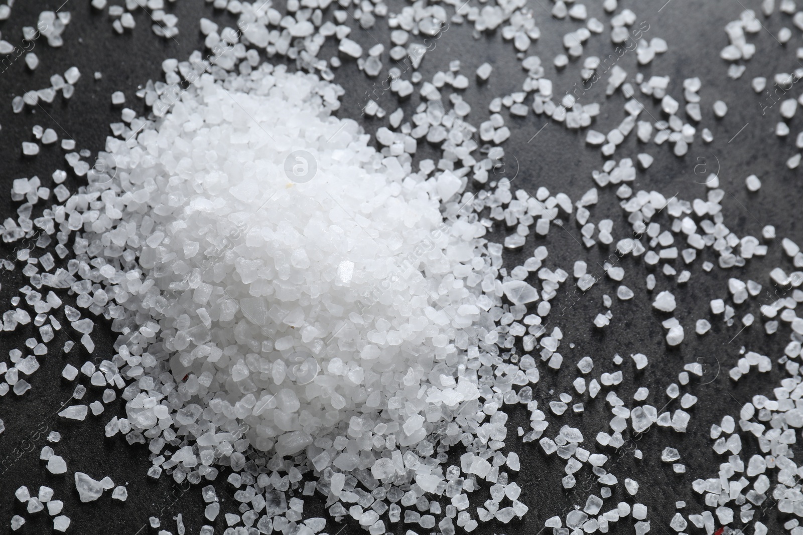 Photo of Heap of natural salt on black table, top view