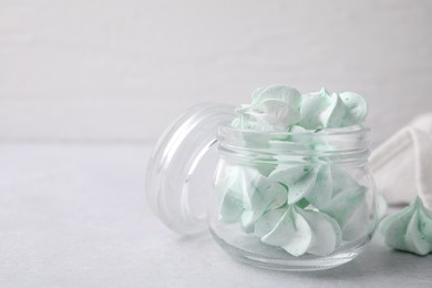 Photo of Tasty meringue cookies in glass jar on light grey table. Space for text