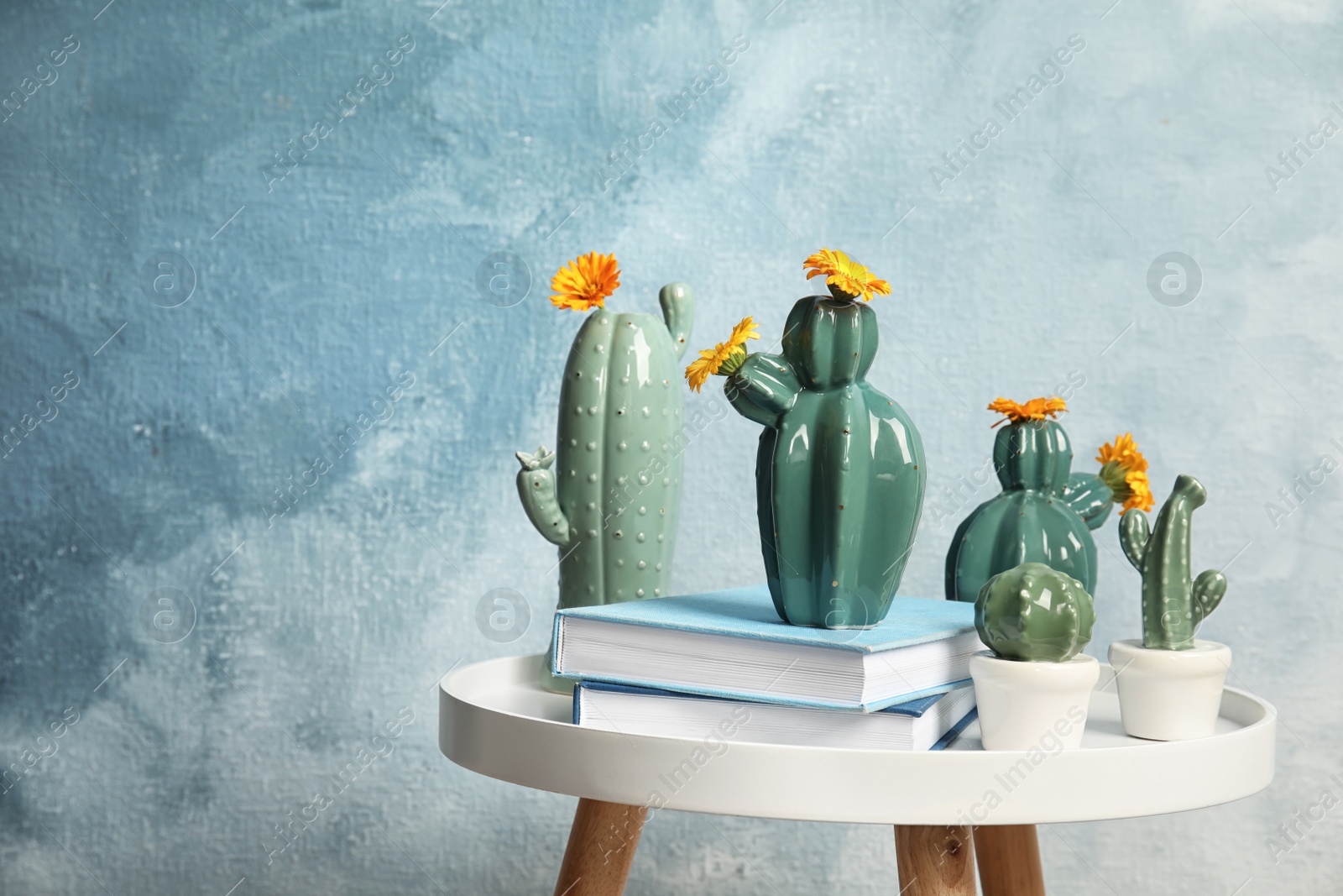 Photo of Trendy cactus shaped vases and books on table against color background. Creative decor