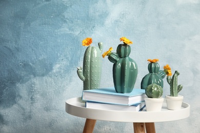 Trendy cactus shaped vases and books on table against color background. Creative decor